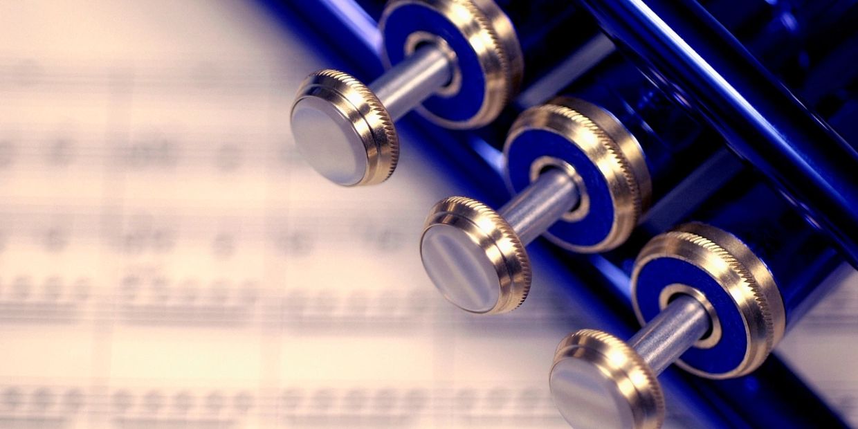 Close-up of trumpet valves with blurred sheet music background.