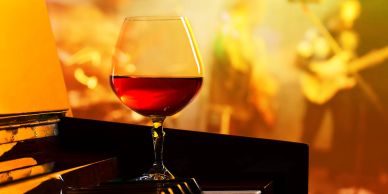 Glass of red wine on piano with blurred musician in warm light.