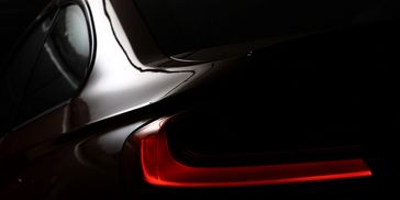 Close-up of a car's sleek rear with illuminated tail light in low light.