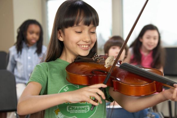 Girl happily playing the violin in a classroom.