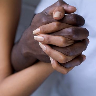 Two hands of two black people, one male, one female, are entwined.