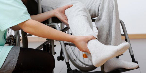 Caregiver assisting elderly person in wheelchair with leg support.