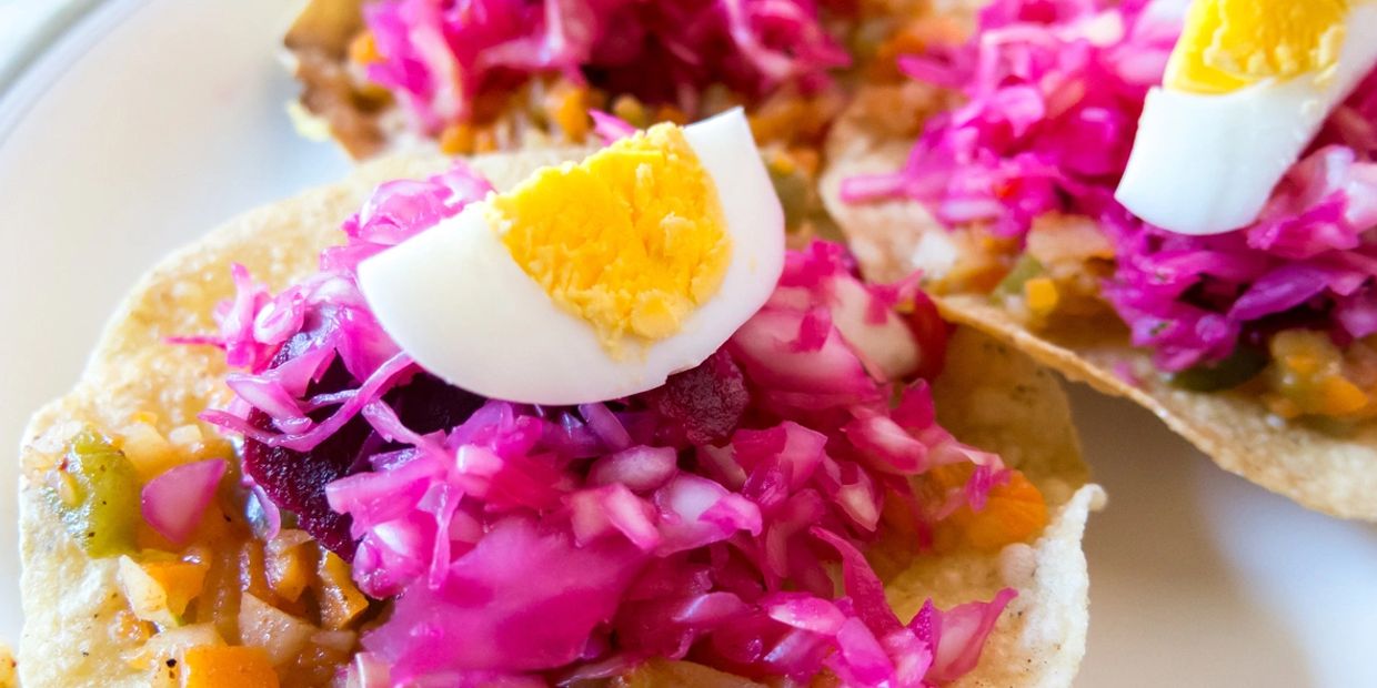 Tostada topped with pickled cabbage and a quartered boiled egg.