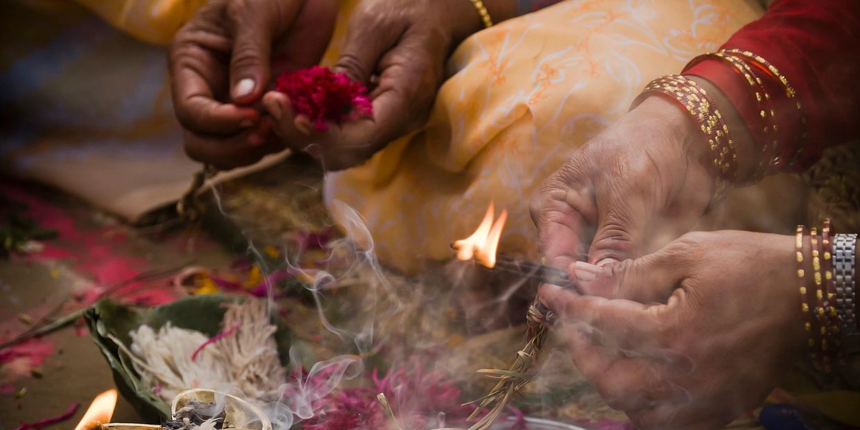 Hands performing a traditional ritual with fire and flowers.