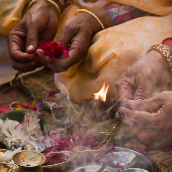Hands holding flowers and lighting a ritual fire in a traditional ceremony.