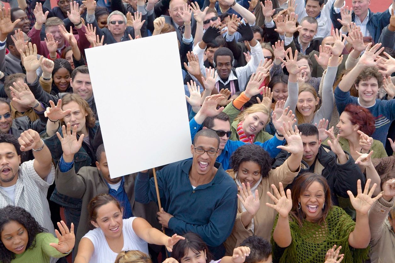 A crowd of people show their hands, in participation of an event, smiling.