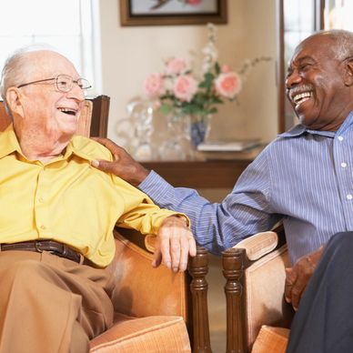 Two elderly men share a joyful moment while sitting and laughing together.