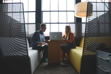 Two colleagues discussing work on a laptop in a modern office booth.