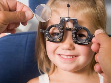 A young girl smiling during an eye exam with a phoropter.
