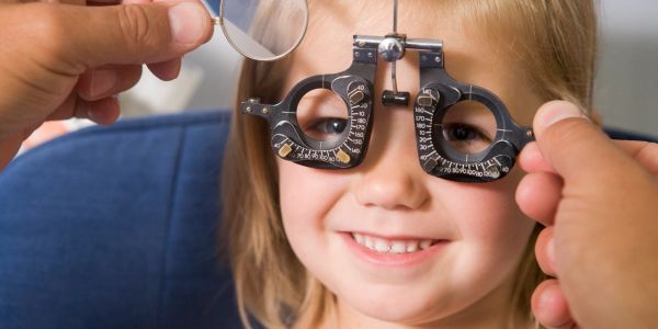 A young girl smiling during an eye exam with a phoropter.