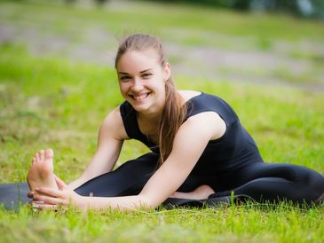 Young woman stretching outdoors on grass.