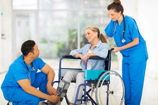 Two physicians speaking to a patient in a wheelchair.