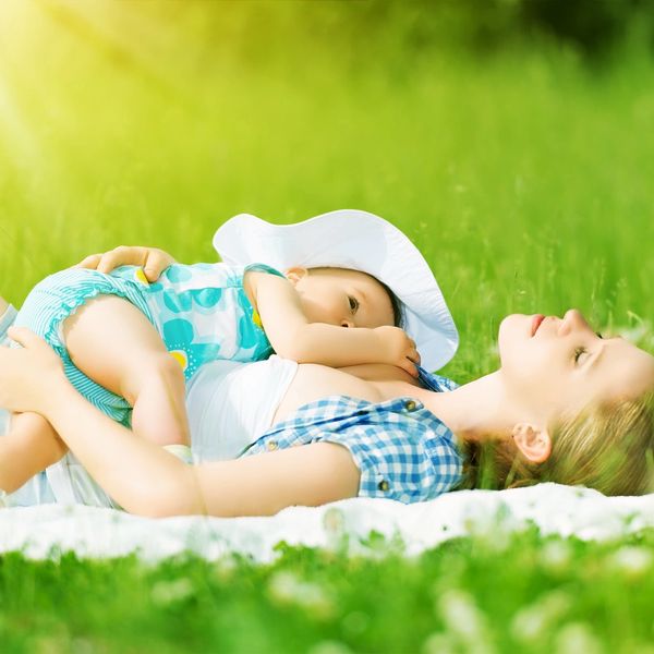 A mother and her baby lying on a blanket in the grass while breastfeeding. Infant looking up at mom