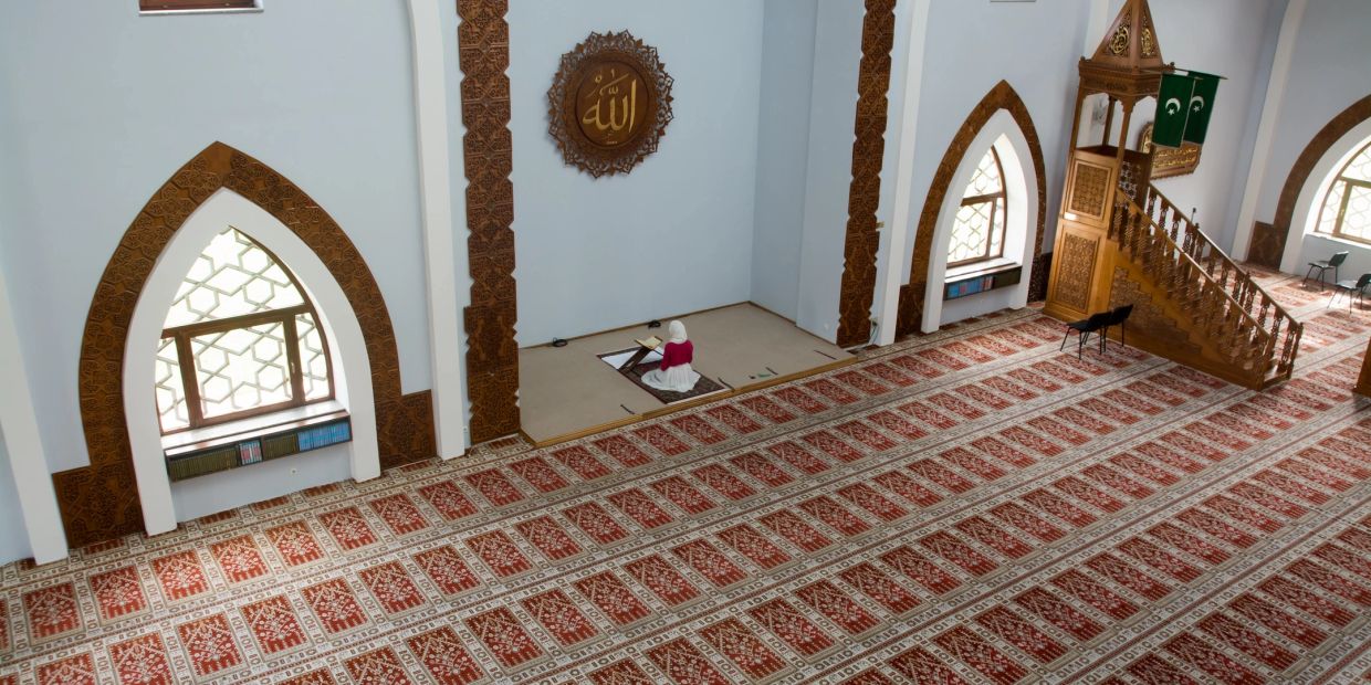 A woman praying alone inside a spacious mosque.
