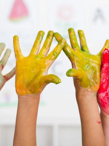 Children's hands covered in colorful paint, raised up.