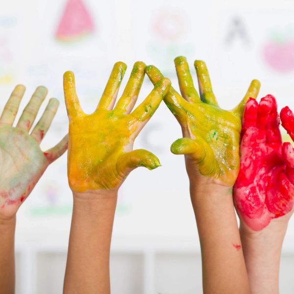 Children's hands covered in colorful paint raised high in the air.