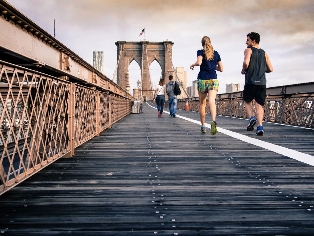 People jogging and walking on the Brooklyn Bridge during the day.