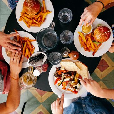 Four diverse friends eating burgers and fries & a quesadilla with the focus on their food and hands