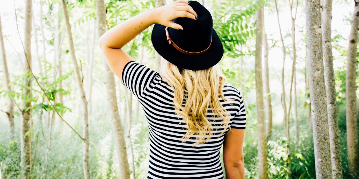Woman in striped shirt and black hat standing in a forest.