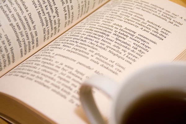 Open book with text and a blurred cup of tea in foreground.