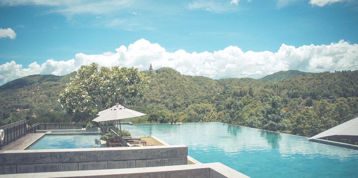 Infinity pool overlooking lush green hills under a bright blue sky.