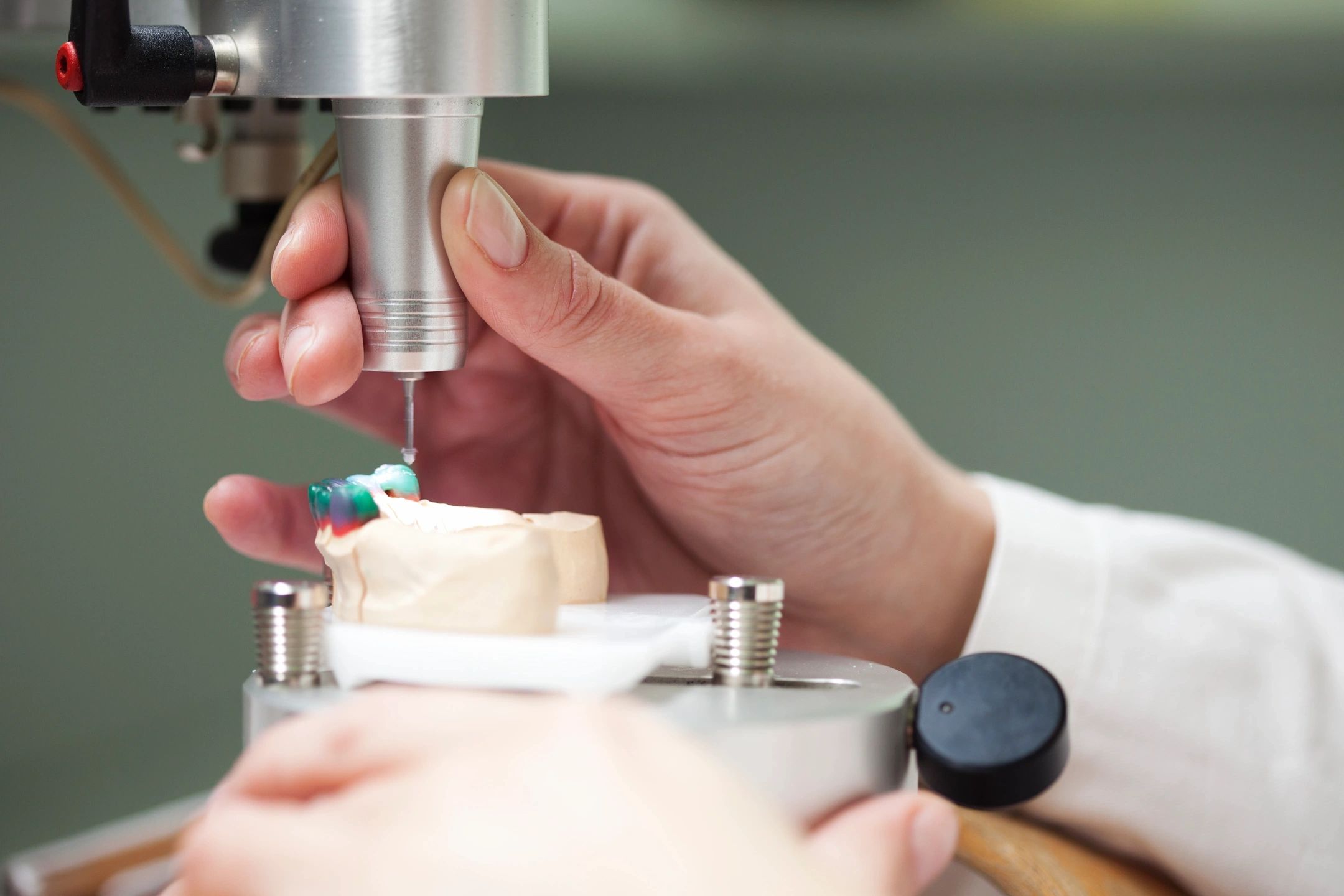 Hand working on a dental mold with a precision tool.