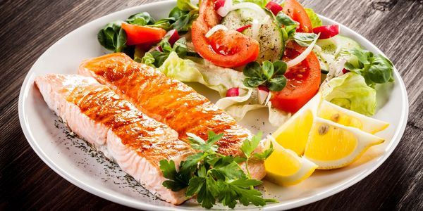 Grilled salmon with fresh salad and lemon wedges on a white plate.