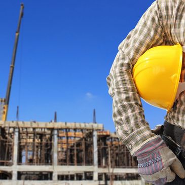 Construction worker holding a yellow helmet at a building site.