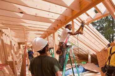 Three construction workers building a wooden house frame.