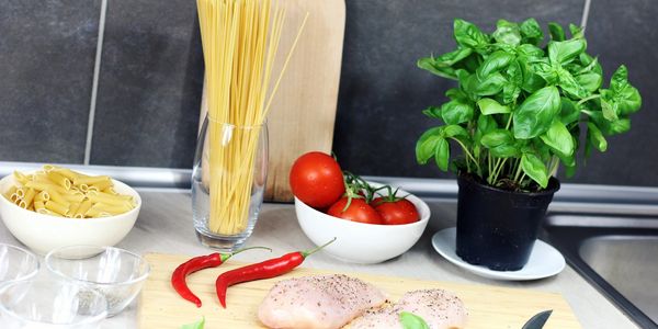 Ingredients for an Italian meal including chicken, pasta, tomatoes, basil, and chili peppers.