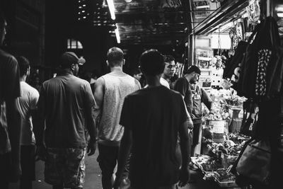 Black and white photo of people walking in a crowded market alley.