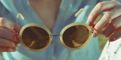 Person holding round sunglasses with a beige frame.