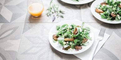 Fresh green salad with mushrooms on white plates and a glass of juice.