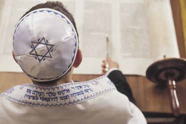 A boy wearing a kippah reads a Torah scroll during a religious ceremony.