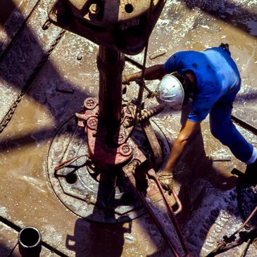 Worker in blue uniform operating drilling equipment on muddy ground.