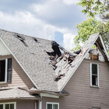 House with a large damaged roof and broken windows under a cloudy sky.