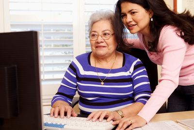 A young woman helping an elderly woman use a computer.