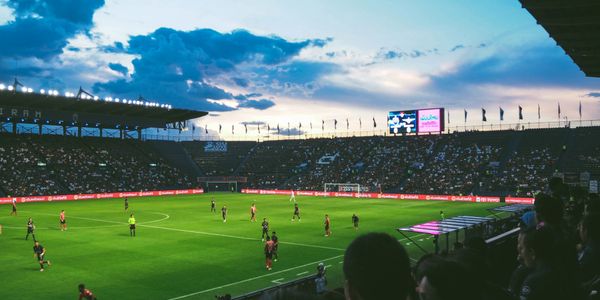 A soccer match under a dramatic evening sky in a packed stadium.