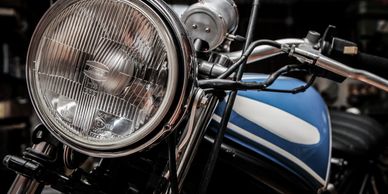 Close-up of a vintage motorcycle's headlight and blue fuel tank.