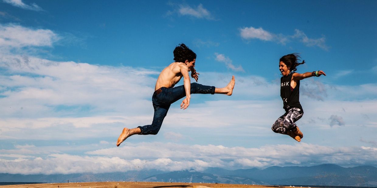 Two people joyfully jumping mid-air against a blue sky.