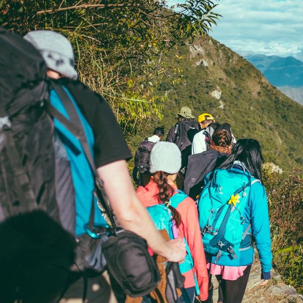 Group of hikers trekking through a mountainous trail under clear skies.