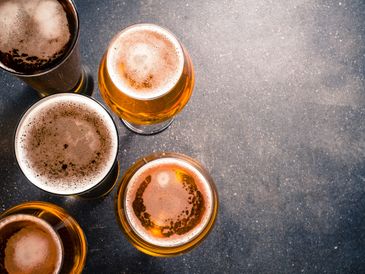 Top view of five glasses filled with beer on a dark surface.