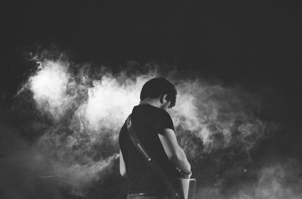 Musician playing guitar amidst stage smoke.