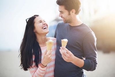 Couple joyfully sharing ice cream cones outdoors on a sunny day.