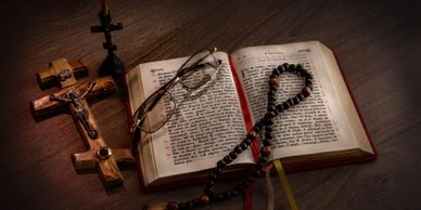 An open Bible with reading glasses, a rosary, and a crucifix on a wooden surface.