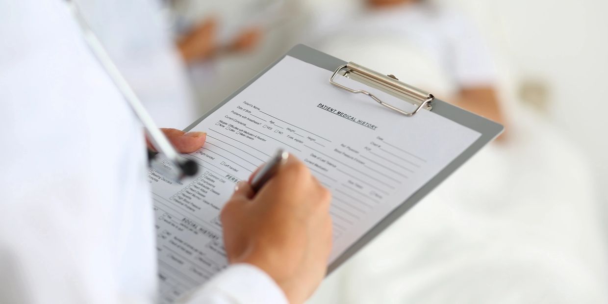 Doctor filling out patient medical history on a clipboard.