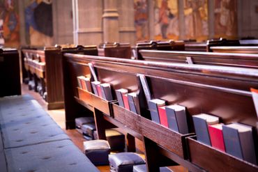 Rows of wooden church pews with hymnals and cushions.