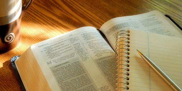 Bible open on a wooden table with notebook, pen, and coffee cup.