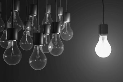One illuminated light bulb stands out among many unlit bulbs in black and white.