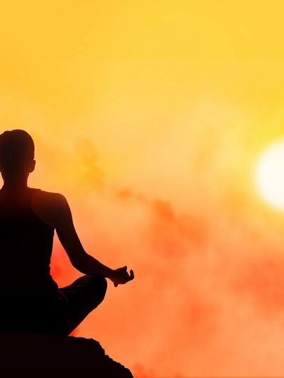 Silhouette of a person meditating at sunset with a vibrant orange sky.